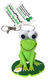 A frog string doll. It has a green body and black and white eyes with a black smile. It is sitting on a green lily pad with a daisy on it. Its tag reads that its name is, "Franny the frog."