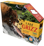 A puzzle box with text that says, "I Am Grizz. Animal-Shaped jigsaw puzzle. Poster size! 1000 pieces. For ages 12+." There is a picture of a Grizzly bear on the side of the box with puzzle pieces coming out of it. The bear is attempting to eat a fish.