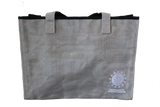 A grey tote bag with the embroidered logo for ISM, which is an anchor sitting on a wave encompassed by a circle that is surrounded by stars, and the words, "Independence Seaport Museum."