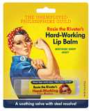 Rosie the Riveter themed lip balm. The packaging is yellow with a picture of Rosie the Riveter off to the side. She has pale skin, brown hair, her iconic blue shirt, and red and white polka-dotted headband. There is text on the packaging that says, "The Unemployed Philosopher's Guild. Rosie the Riveter's Hard-Working Lip Balm. Machine shop Mint." The lip balm itself has a yellow covering on it with Rosies face. It says, "Your lips will say, 'We Can Do It!' Rosie the Riveter's Hard-Working Lip Balm."
