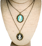 A blue and black pendant on a necklace chain, each with a white mermaid in the center of them. The outside is gold with an ornate design.