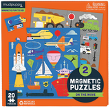 A box for two magnetic puzzles. One is a blue puzzle with a rocket, a ship, an airplane, a helicopter, a submarine, and a paraglider. Another is a grey puzzle that is being partially covered by the first puzzle, but we can see that there is a train, a dump truck, and cars on it, along with a traffic light. The box itself is orange and has text saying, "Mudpuppy. Magnetic fun to go! 2 magnetic puzzles. On the move."
