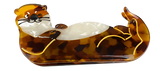 A hair clip shaped like an otter. It has a white belly and a body with different shades of brown. Its limbs are outlined in yellow. It is winking with a playful expression.