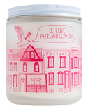 A candle with an illustration of different houses with a bird flying over them, stating "I love Philadelphia." The illustration has a sketchy style done in pink.