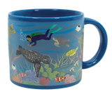 A blue mug with illustrations of sea turtles, fish, a shark, a scuba diver, coral, and other sea life in the ocean.
