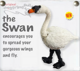 A string doll shaped like a swan. It has a white body, black legs and face, and an orange beak. There is text next to it that states, "The Swan encourages you to spread your gorgeous wings and fly."
