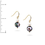 Pair of earrings with floral designs and pearls next to a ruler for scale on a white background