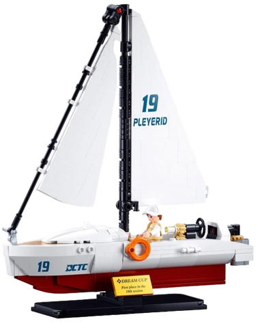 Model sailboat with white sail and red hull, displayed in front of its packaging.