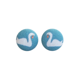 A pair of round stud earrings featuring a swan design, with a white swan and orange beak on a textured light blue background