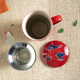 Red mug with a metal filter and decorative lid on a textured surface