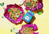 Three purple cabbage bowls filled with a salad and a container of Spicewalla Chinese Five Spice on a yellow background.