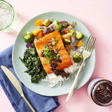 Plate of salmon with vegetables and rice on a pink background