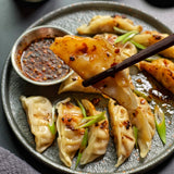 Garnished potstickers on a plate with dipping sauce