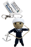 A string doll with a white cap and a blue sailor uniform, holding an anchor on a piece of rope. His tag reads that his name is Anchors.