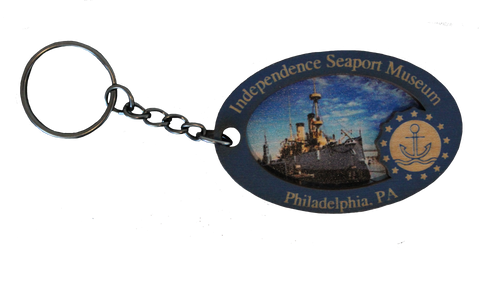 A wooden keychain that shows an image of the Cruiser Olympia on it, along with text that says, "Independence Seaport Museum. Philadelphia, PA," along with the ISM logo, which is an anchor floating on some waves encompassed in a circle and surrounded by stars. 