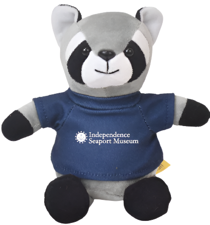 A small plush raccoon wearing a shirt that says "Independence Seaport Museum" with a logo of an anchor that is surrounded by a circle with stars around the outside of it.